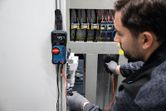 Una persona che indossa un equipaggiamento di sicurezza utilizza un multimetro digitale per testare un quadro elettrico.
