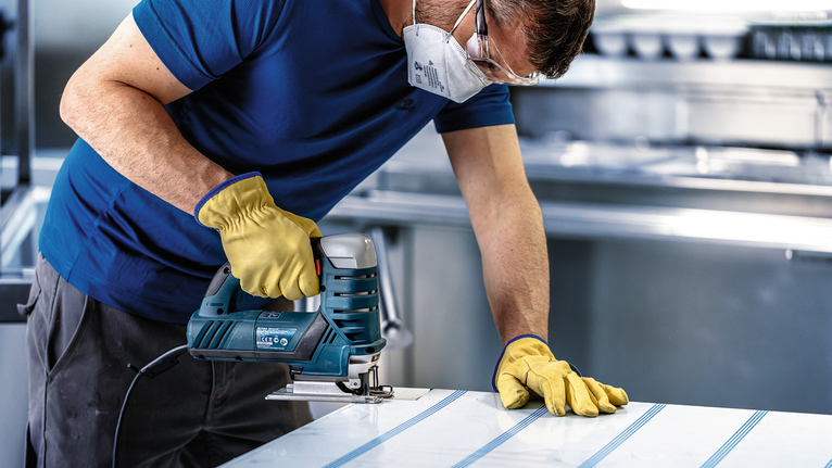 Una persona che indossa dispositivi di sicurezza utilizza un seghetto alternativo per tagliare il materiale in fogli.