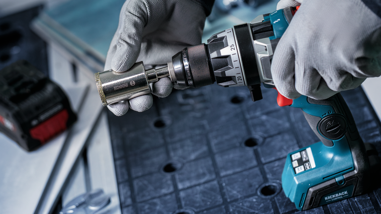 Una persona che indossa un equipaggiamento di sicurezza collega una presa a un trapano a batteria.