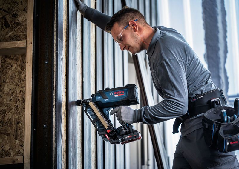 Una persona che indossa un equipaggiamento di sicurezza utilizza una chiodatrice per legno senza fili su un telaio a parete.