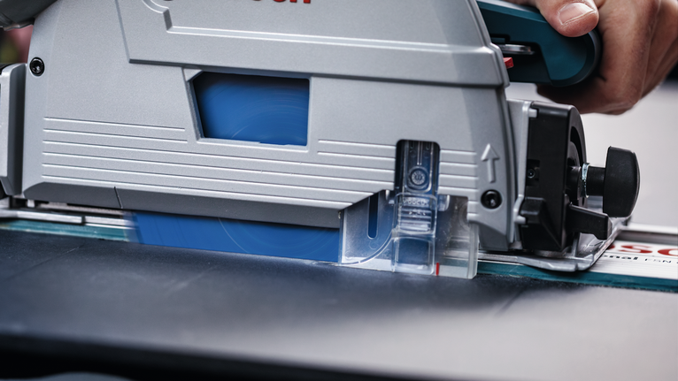 Una persona guida una sega circolare lungo un binario per tagliare un pezzo di legno.