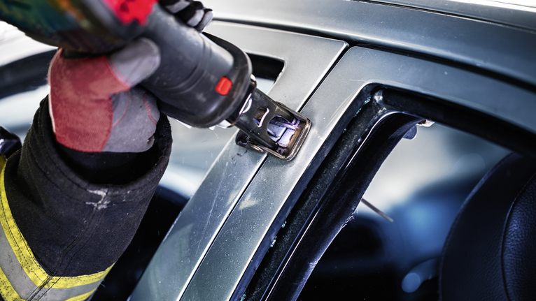 Una persona che indossa un equipaggiamento di sicurezza utilizza un elettroutensile per tagliare il telaio di un'auto.