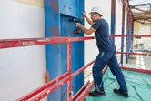 Una persona che indossa un equipaggiamento di sicurezza utilizza una chiave a impulsi senza fili su una trave d'acciaio.