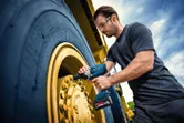 Una persona che indossa un equipaggiamento di sicurezza utilizza una chiave a impulsi senza fili su una ruota di un veicolo di grandi dimensioni.