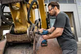 Una persona che indossa dispositivi di sicurezza utilizza una chiave a impulsi a batteria su macchinari pesanti.