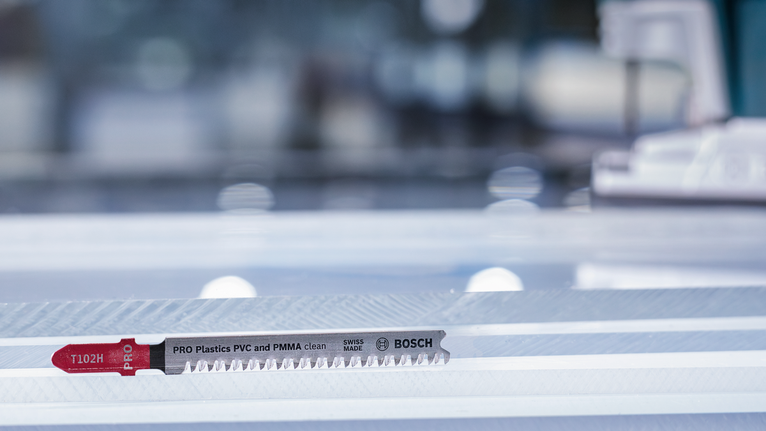 La lama del seghetto alternativo per tagliare la plastica poggia su una superficie di lavoro a strisce.