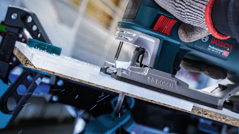 Una persona che indossa un equipaggiamento di sicurezza aziona un seghetto alternativo per tagliare un foglio di materiale.