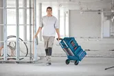 Una persona traina un carrello pieghevole con cassette degli attrezzi accatastate in un cantiere edile.