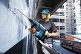 Una persona che indossa un equipaggiamento di sicurezza utilizza un martello perforatore per rompere il cemento in un cantiere edile.