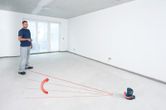 Una persona utilizza uno strumento di livellamento laser proiettando linee attraverso una stanza vuota.