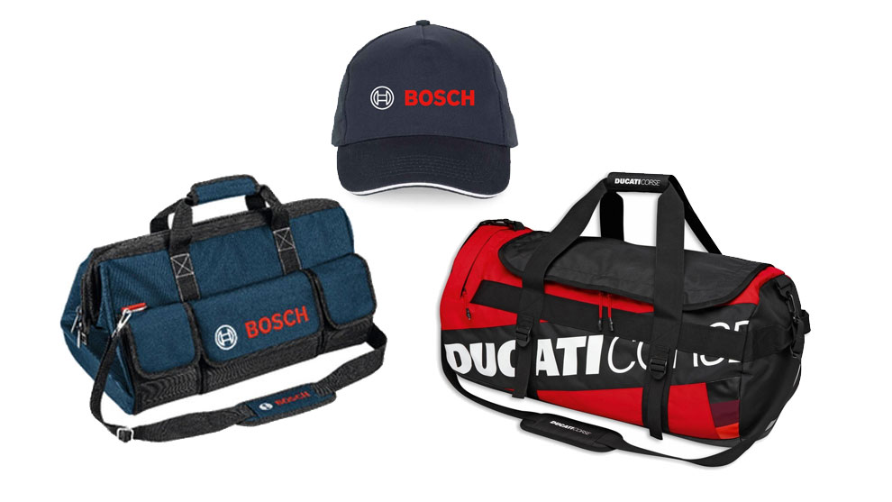 Tre oggetti visibili: una borsa blu con logo Bosch, un cappellino blu con logo Bosch, e una borsa rossa e nera con logo Ducati. I colori predominanti sono blu, rosso e nero. Gli oggetti sono disposti su uno sfondo bianco.