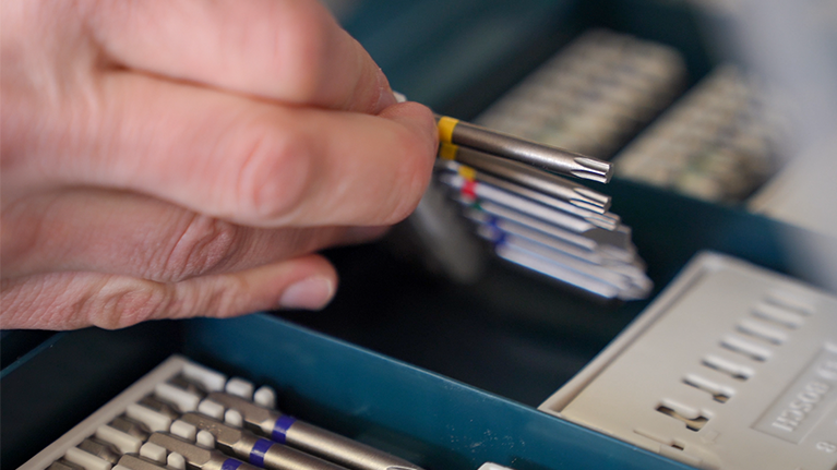 Una mano seleziona punte di trapano in una cassetta blu.