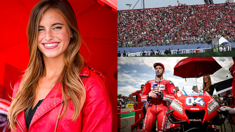 Una donna sorridente in giacca rossa davanti a un pubblico in festa e un pilota Ducati.