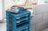 صناديق أدوات زرقاء مكدسة مع صينية تنظيم مفتوحة تحتوي على مسامير ومقابس حائط بالقرب منها.