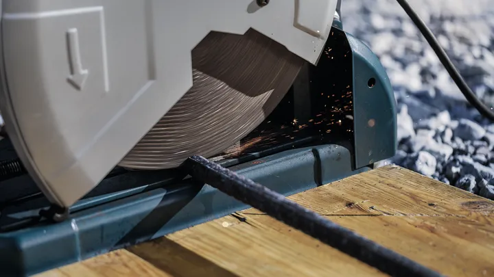 منشار قطع يقطع قضيبًا معدنيًا على سطح خشبي.