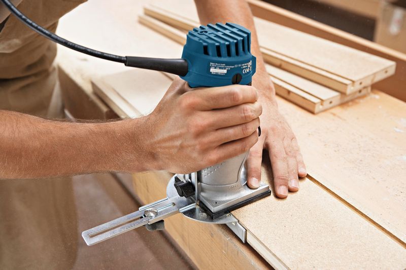 A person uses a palm router to shape the edge of a wooden board.