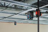 Laser leveling tool projecting red guidelines across a suspended ceiling grid.