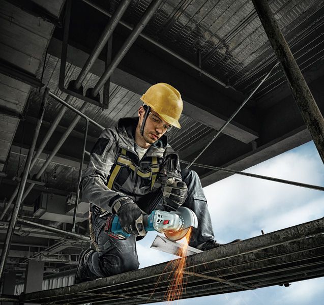 A person wearing safety equipment uses an angle grinder to cut metal scaffolding.