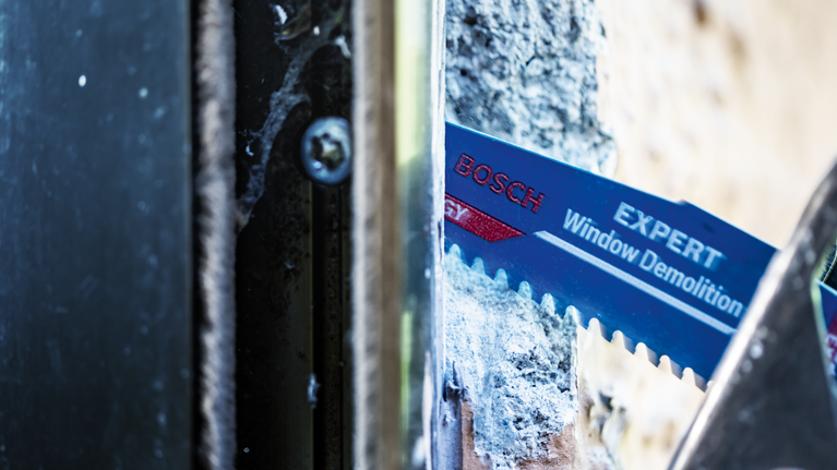 Reciprocating saw blade cuts through a window frame during demolition work.
