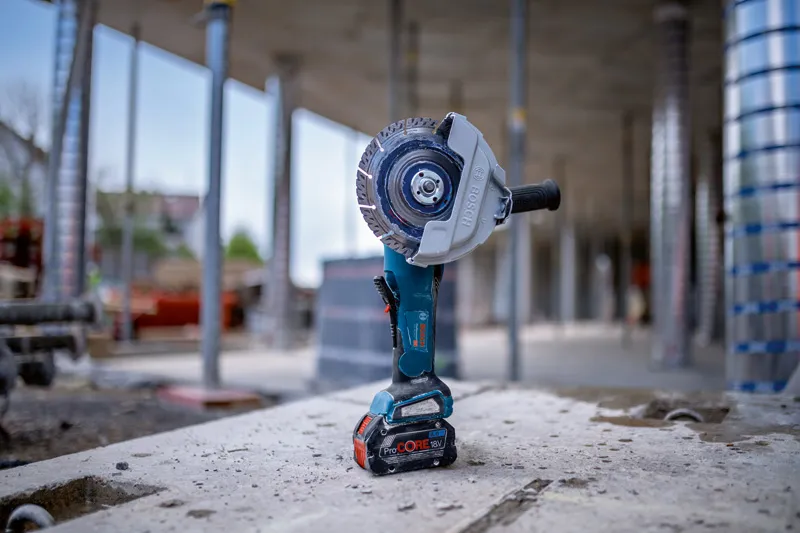 Cordless angle grinder standing upright on a concrete surface at a construction site.