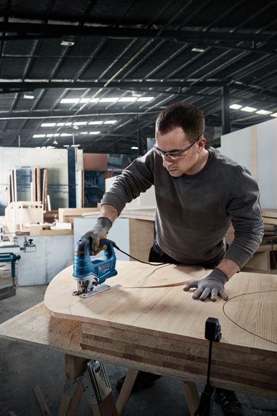 Person wearing safety equipment uses a jigsaw to cut curved shapes in plywood.