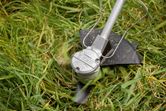 Cordless brushcutter trims tall grass with spinning blade.