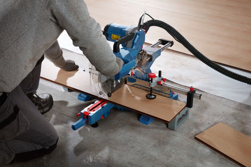 A person wearing safety equipment cuts laminate flooring with a sliding miter saw.