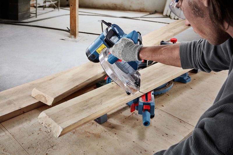 A person wearing safety equipment uses a circular saw to cut wooden planks.