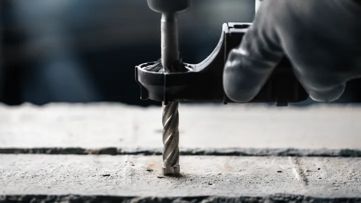 Person wearing safety equipment drills into concrete.