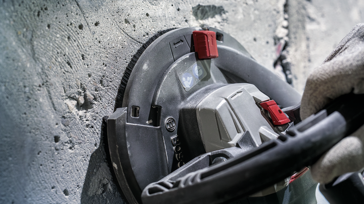 Person wearing safety equipment grinds a concrete wall with a power tool.