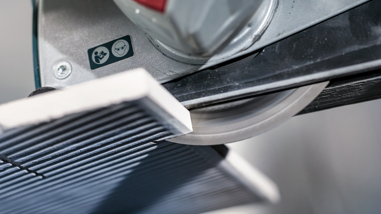 Tile cutter slicing a ceramic tile in a workshop.
