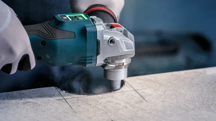 Person wearing safety equipment uses a power tool to cut a circular hole in stone.