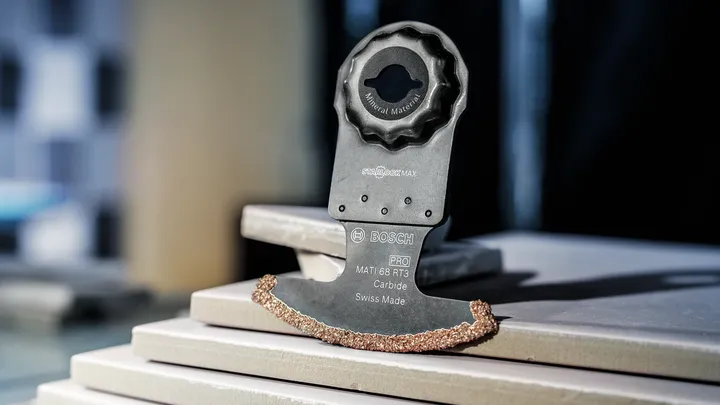 Oscillating tool blade with carbide edge rests on stacked ceramic tiles.