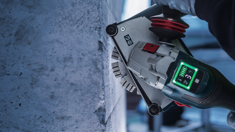 A person wearing safety equipment uses a wall chaser to cut grooves in concrete.