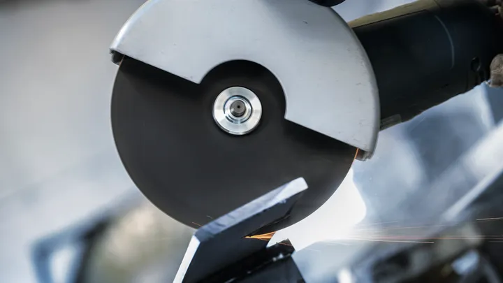 A person wearing safety equipment uses an angle grinder to cut metal.