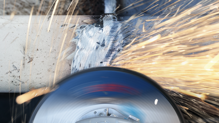 Angle grinder cutting metal pipe, creating sparks.