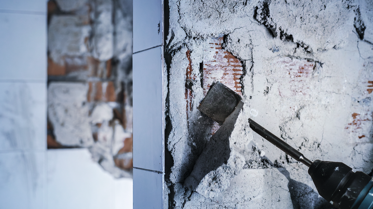 Demolition hammer chipping plaster from a brick wall.