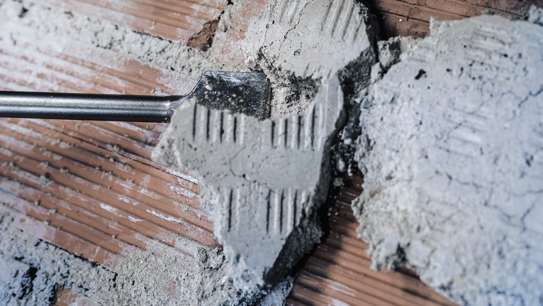 Chisel removing mortar from tile surface.