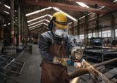 A person wearing safety equipment grinds a metal pipe, creating sparks in a workshop.