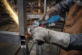 A person wearing safety equipment grinds a metal frame with an angle grinder.
