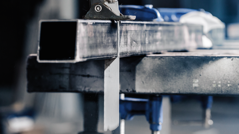 Band saw cutting through a metal beam secured in a workshop.