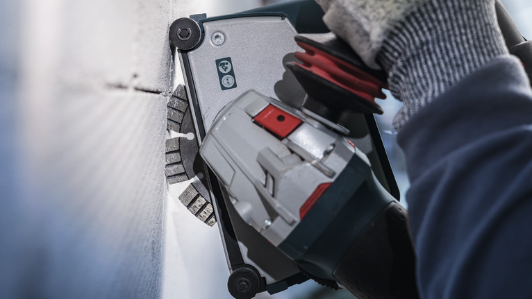 Person wearing safety equipment uses a power tool to cut into a wall.