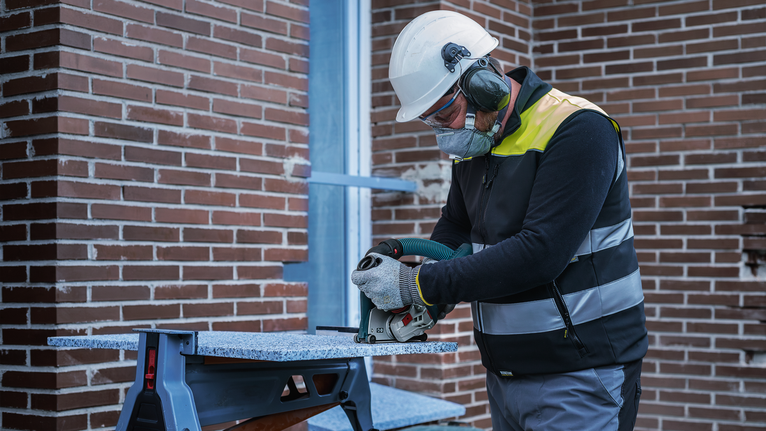 A person wearing safety equipment cuts stone with a circular power saw.