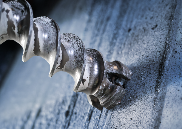 Close-up of a spiral drill bit boring into a concrete wall.