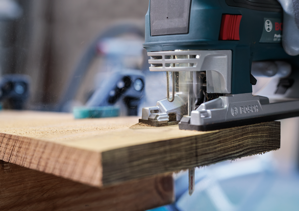 Jigsaw cutting through a thick wooden plank in a workshop.