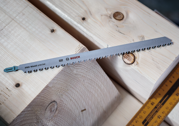 Long jigsaw blade rests on stacked wooden beams beside a measuring ruler.