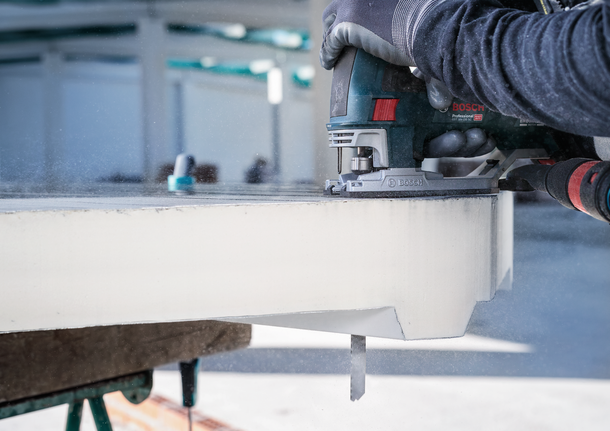 Person wearing safety equipment uses a jigsaw to cut a thick slab.