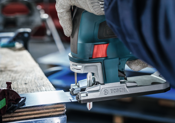 A person wearing safety equipment uses a jigsaw to cut a metal sheet.