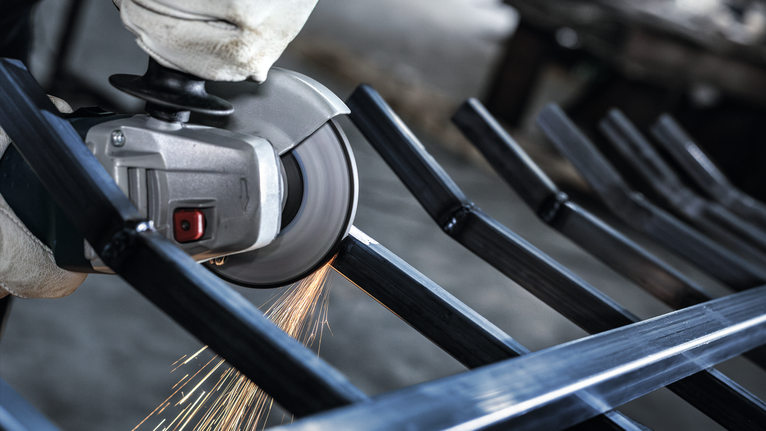 Person wearing safety equipment grinds metal bars, producing sparks.
