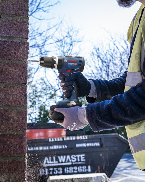 A person wearing safety equipment drills into a brick wall with a cordless power drill.